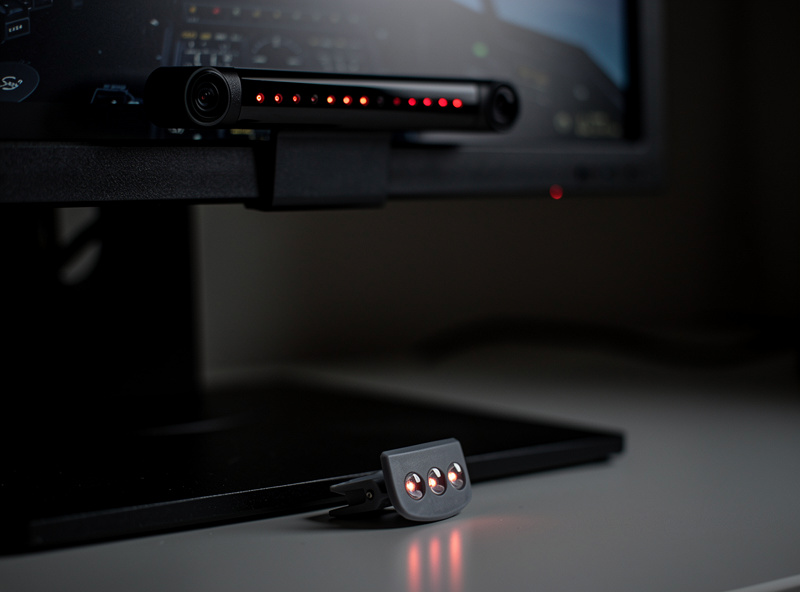 An infrared head-tracking camera bar mounted on top of a flight sim monitor with a headset clip nearby