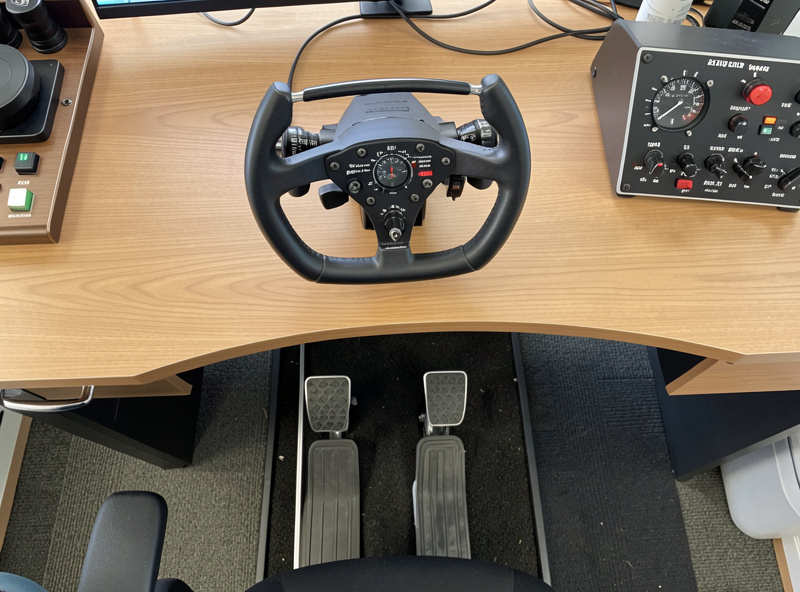Overhead view of a yoke mounted to a desk next to rudder pedals and a throttle quadrant on a home flight sim setup